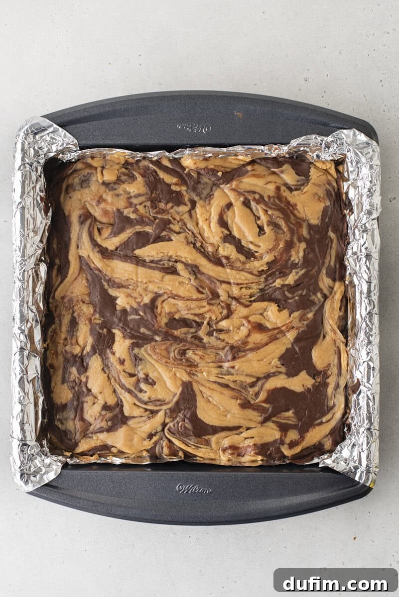 Decadent Chocolate Peanut Butter Fudge 16 A square baking pan lined with foil holds a batch of brownies with swirled chocolate and peanut butter patterns on top, viewed from above.