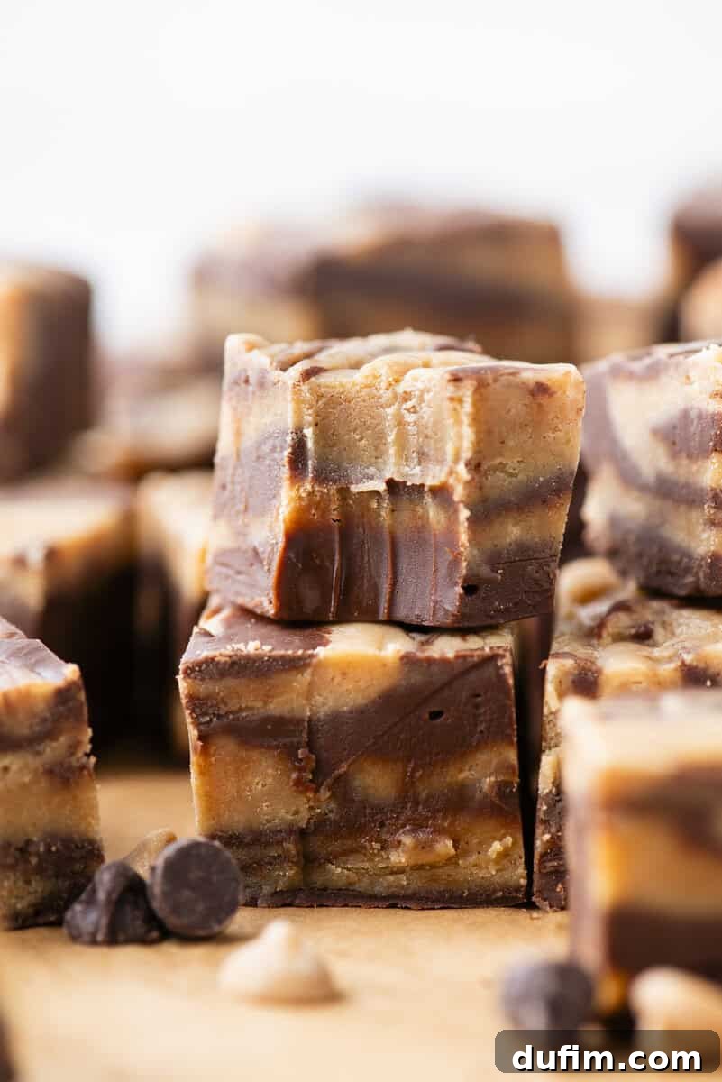 Decadent Chocolate Peanut Butter Fudge 17 Close-up of stacked squares of chocolate and peanut butter fudge with visible swirled layers, set on a wooden surface with scattered chocolate and peanut butter chips in the foreground.