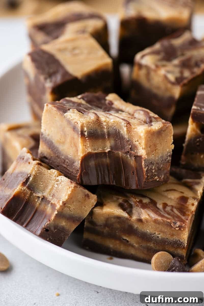 Decadent Chocolate Peanut Butter Fudge 18 A close-up of several pieces of layered chocolate and peanut butter fudge stacked in a white bowl. The fudge has a marbled appearance with distinct swirls of brown and tan.