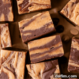 Several pieces of swirled chocolate and peanut butter fudge are arranged on a brown surface, showcasing their marbled layers and rich, creamy texture.
