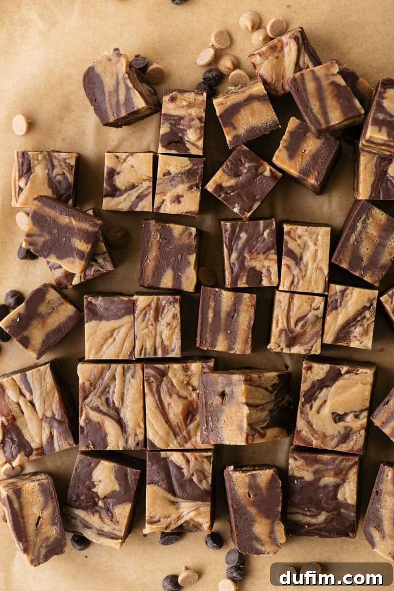 Decadent Chocolate Peanut Butter Fudge 3 Squares of marbled chocolate and peanut butter fudge are arranged on brown parchment paper, with a few scattered chocolate and peanut butter chips around them.