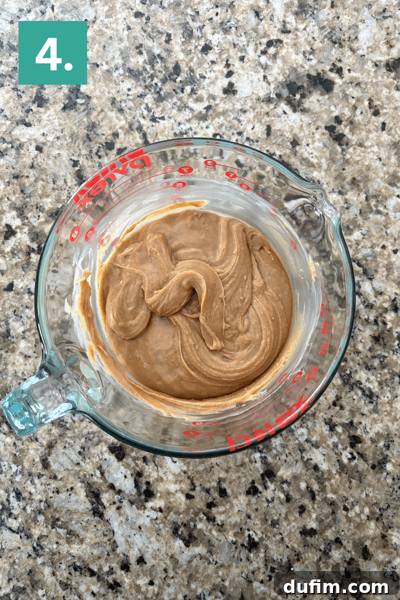 Decadent Chocolate Peanut Butter Fudge 9 A glass measuring cup filled with a creamy, light brown mixture sits on a speckled countertop. A green box with the number 4 in white is in the top left corner.
