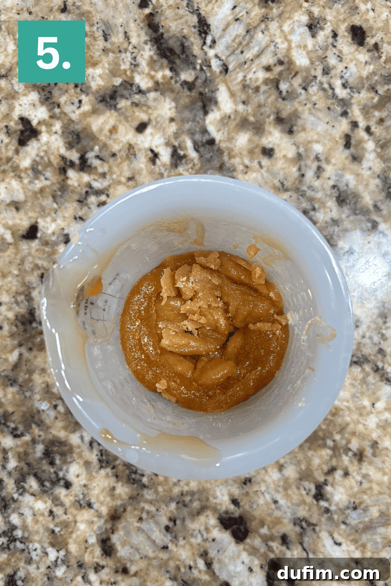 A white mixing bowl on a granite countertop contains an orange-brown paste with crumbly chunks. A green box with the number 5 is in the top left corner of the image.