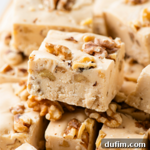 Close-up of creamy fudge squares with pieces of walnuts mixed in and scattered on top, stacked closely together.