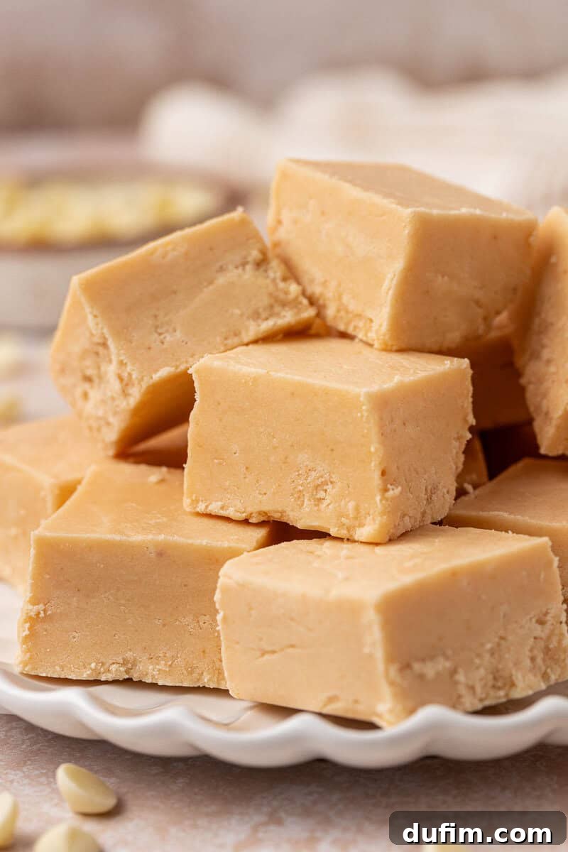 Guaranteed Perfect Vanilla Fudge 12 A plate stacked with creamy, light brown peanut butter fudge squares, with a smooth texture and a few white chocolate chips scattered around on the surface.