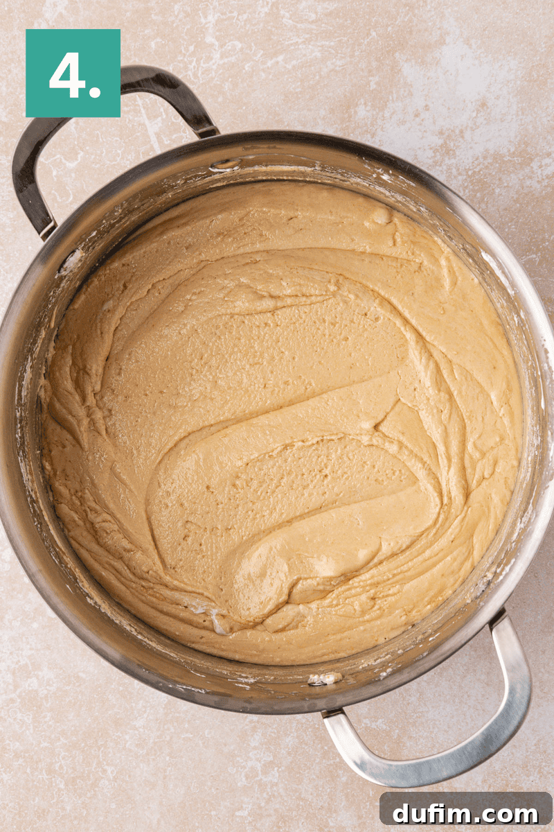 Guaranteed Perfect Vanilla Fudge 7 A large metal mixing bowl filled with smooth, creamy cookie dough sits on a light countertop. A green square with the number 4 is in the upper left corner of the image.