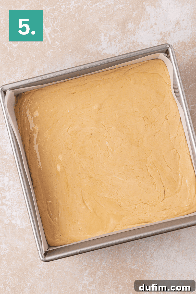Guaranteed Perfect Vanilla Fudge 8 A square baking pan lined with parchment paper, filled with smooth, light brown batter, sits on a light countertop. A green box with the number 5 is in the top left corner.