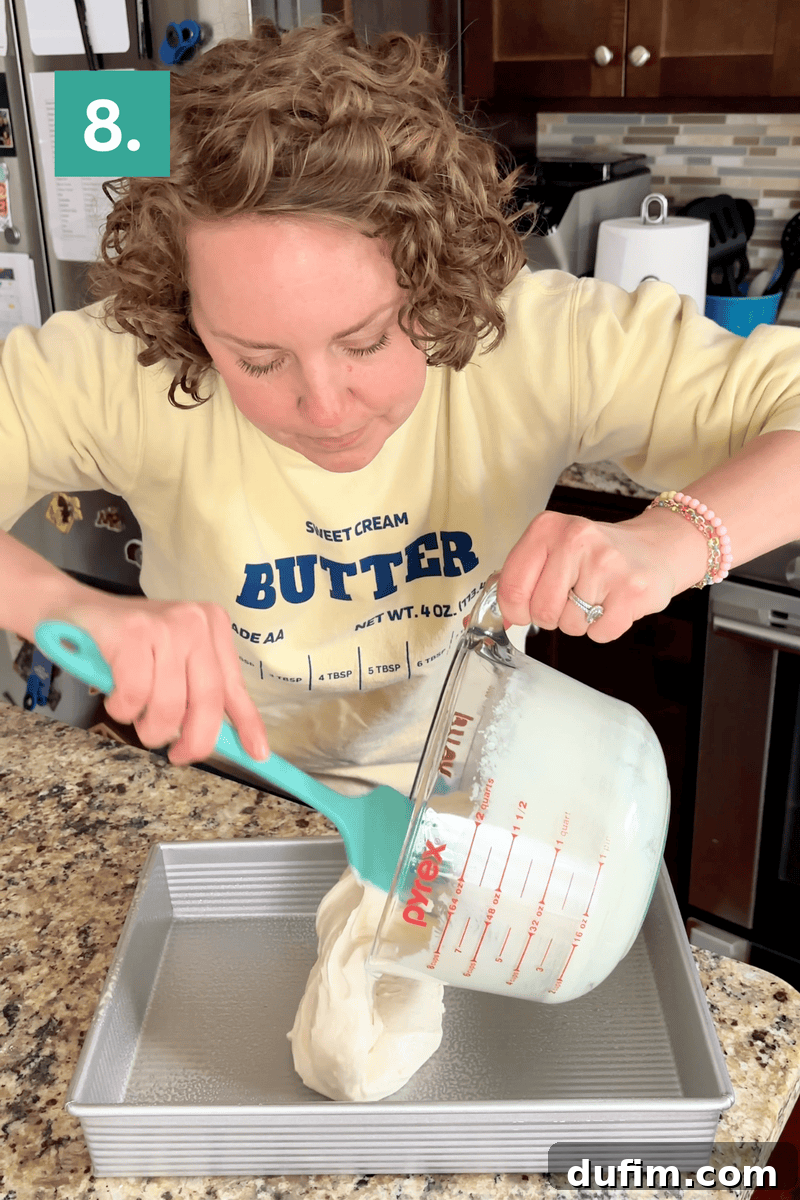 A woman pours a thick white batter from a glass measuring cup into a baking pan on a kitchen counter. She is wearing a yellow sweatshirt that says Sweet Cream BUTTER. A green box with the number 8 is in the top left corner.