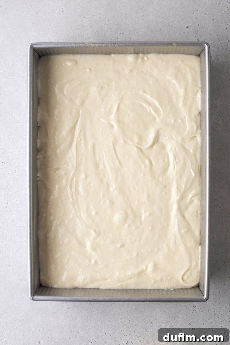 A rectangular metal baking pan filled with smooth, light-colored cake batter sits on a light gray surface, ready to be baked.