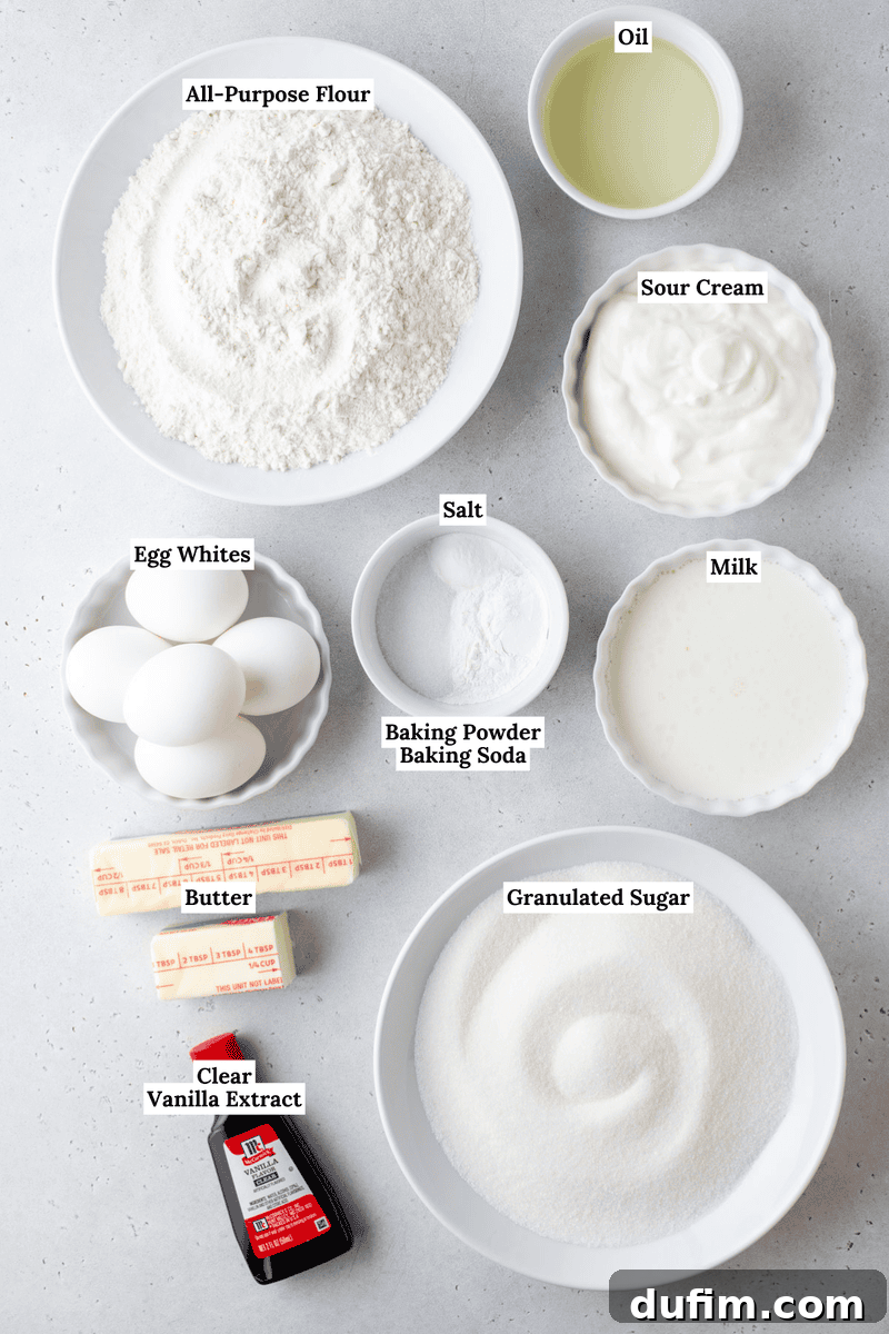 Top-down view of labeled cake ingredients in bowls and plates, including all-purpose flour, oil, sour cream, egg whites, salt, baking powder, baking soda, milk, butter, granulated sugar, and clear vanilla extract.
