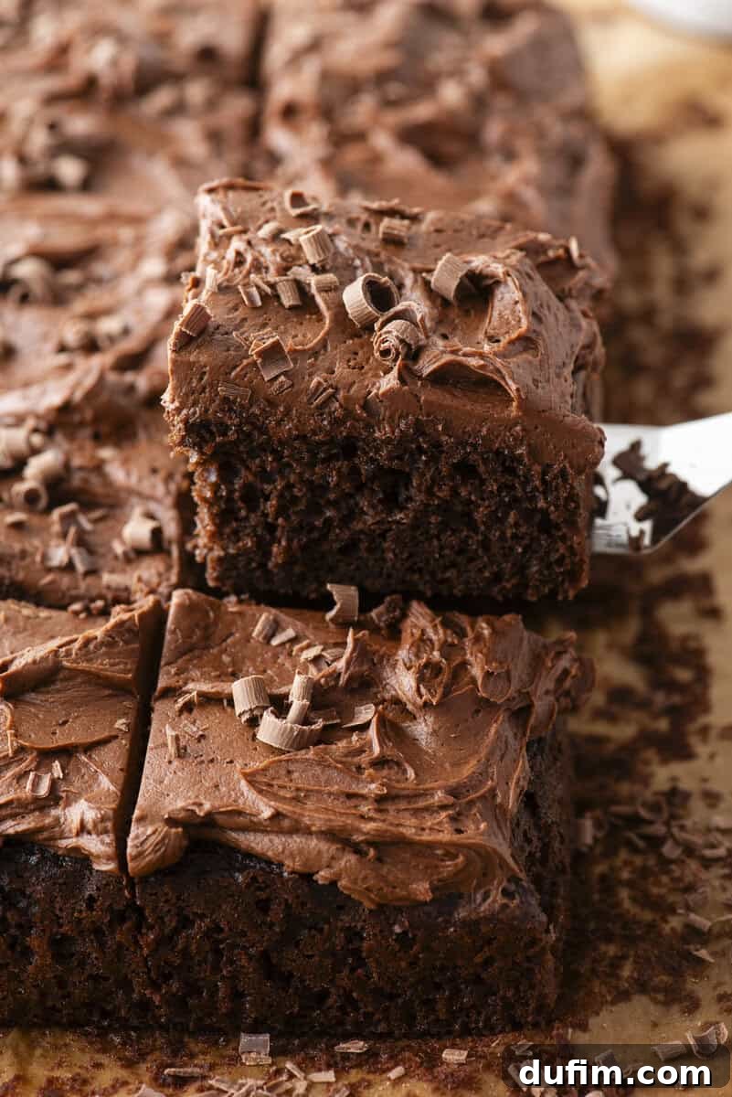 Decadent Homemade 9x13 Chocolate Cake 2 A perfect square slice of moist chocolate sheet cake with a thick layer of chocolate buttercream frosting and chocolate shavings, being lifted from a 9x13 pan.