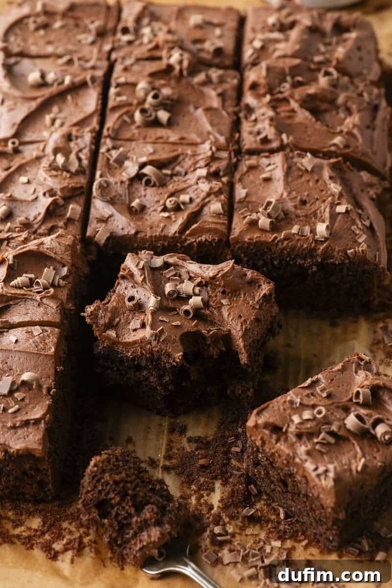 Decadent Homemade 9x13 Chocolate Cake 13 A fork taking a bite out of a square of moist chocolate cake with thick chocolate frosting, showcasing the perfect texture.