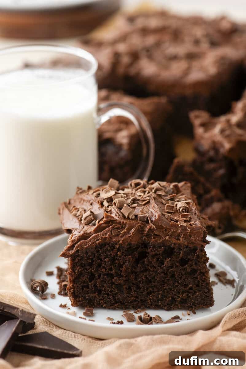 Decadent Homemade 9x13 Chocolate Cake 5 A slice of the ultimate chocolate sheet cake on a white plate next to a glass of milk, showcasing its moist texture and creamy frosting.