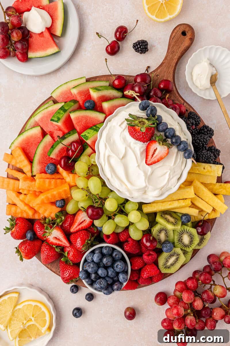 Cream Cheese Fruit Dip Recipe for Parties and Snacks 11 A round wooden board filled with assorted fresh fruits surrounding a bowl of creamy white dip topped with berries.