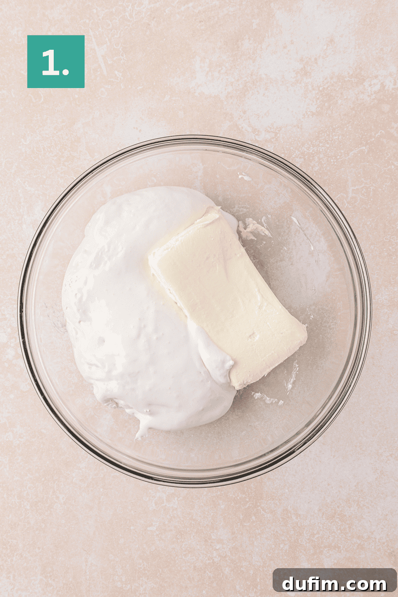 Cream Cheese Fruit Dip Recipe for Parties and Snacks 5 A glass bowl containing a block of cream cheese and a large dollop of marshmallow fluff, on a light countertop.