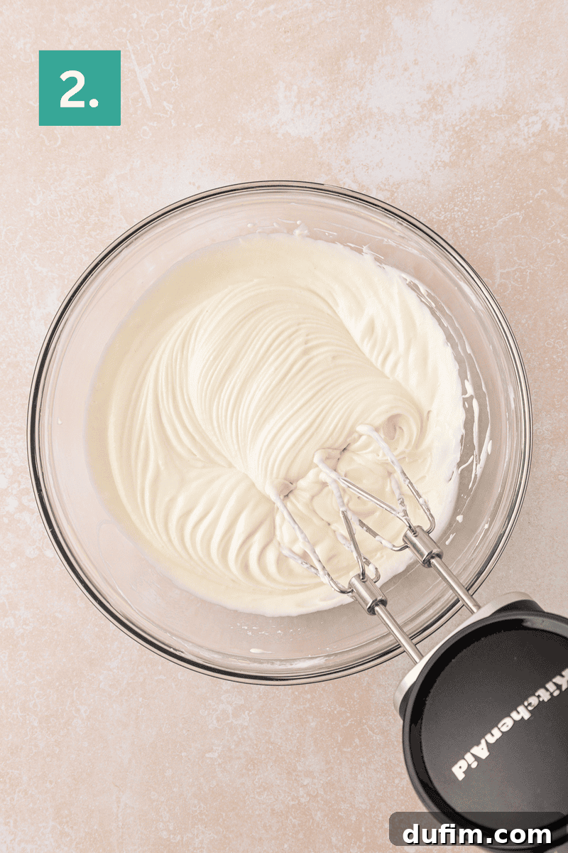 Cream Cheese Fruit Dip Recipe for Parties and Snacks 6 A glass bowl filled with smooth, whipped cream cheese mixture being mixed with an electric hand mixer.