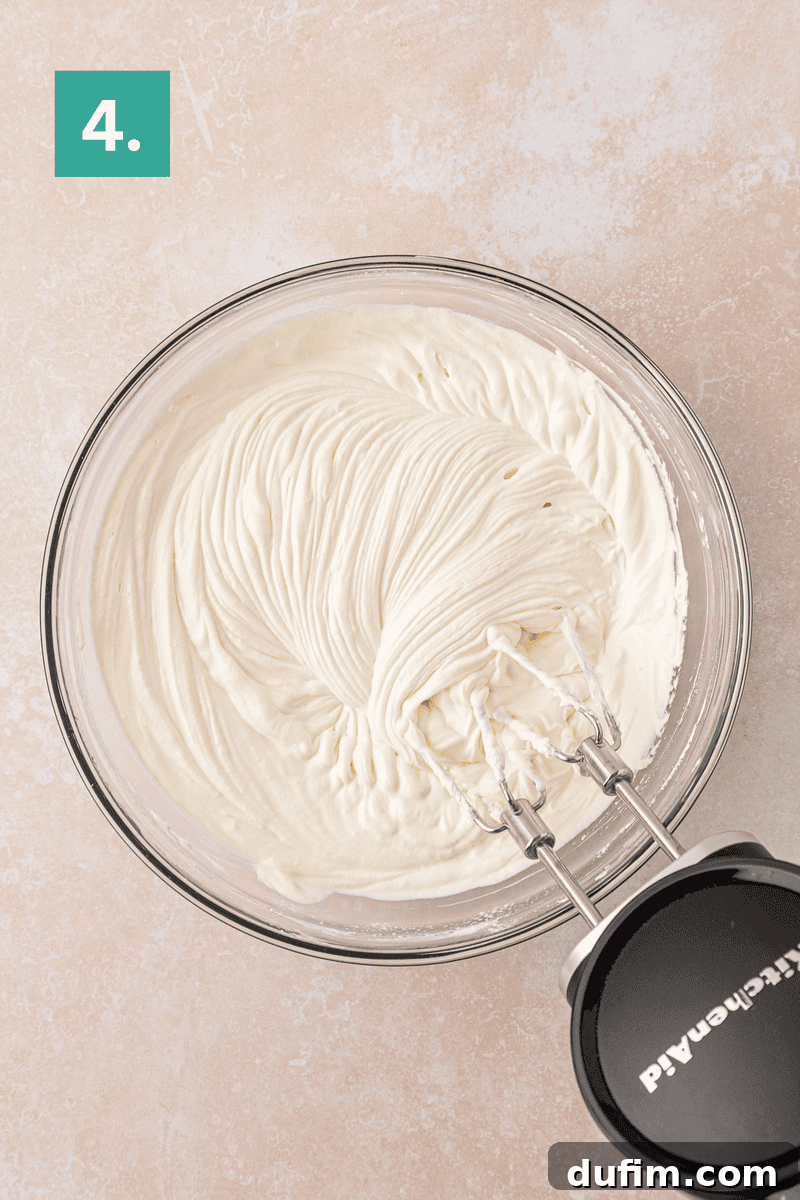 Cream Cheese Fruit Dip Recipe for Parties and Snacks 8 A glass bowl filled with whipped cream and an electric hand mixer on the side.