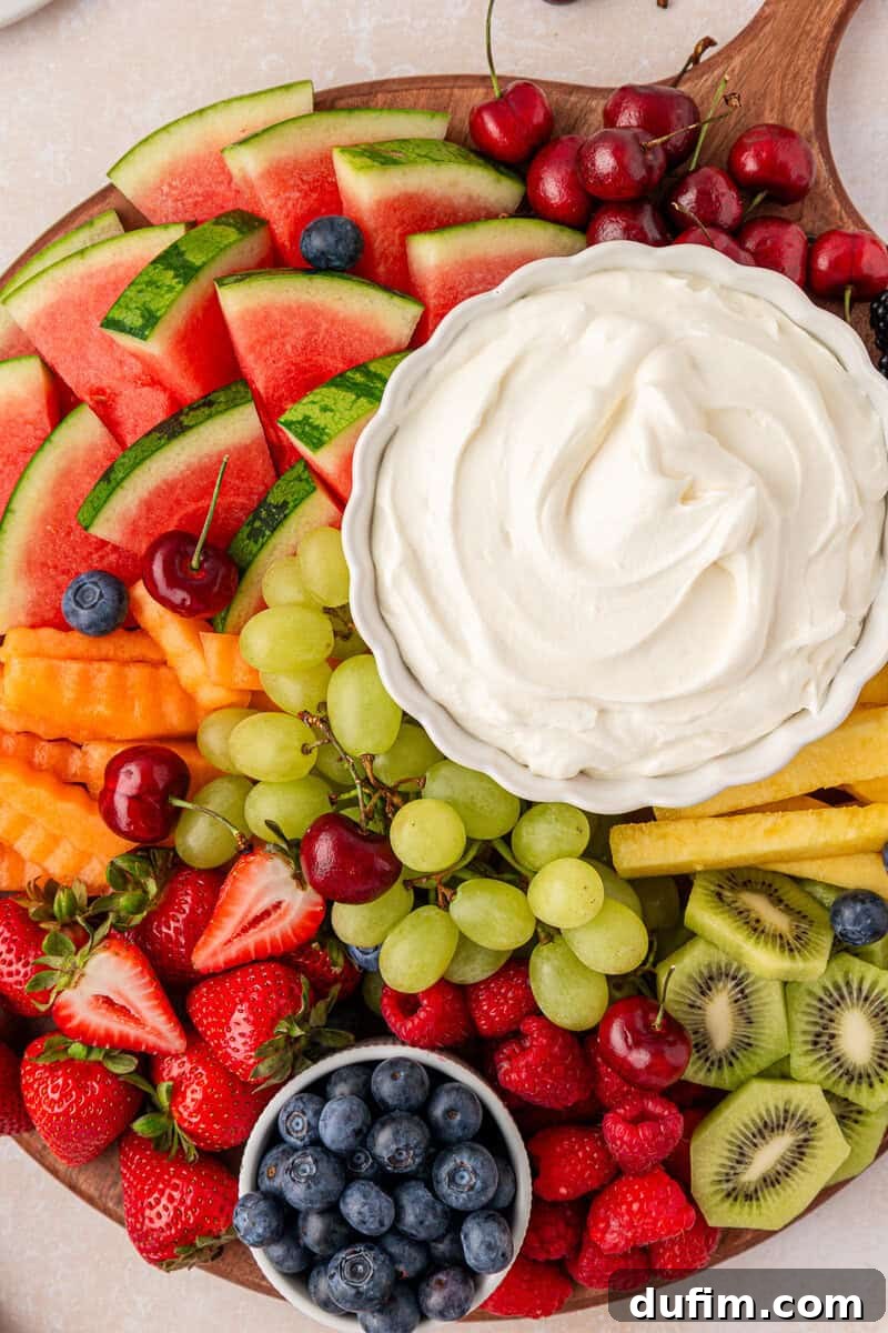 Cream Cheese Fruit Dip Recipe for Parties and Snacks 9 A wooden platter filled with assorted fresh fruits arranged around a bowl of creamy white fruit dip.