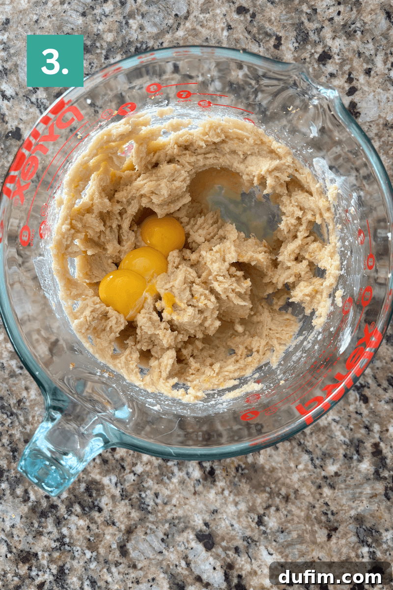 A glass measuring cup containing a creamy batter and three cracked eggs.