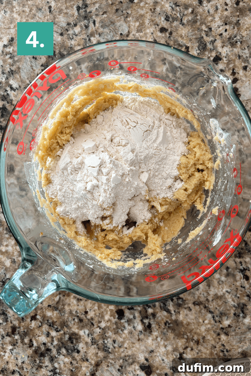 Mixer combining cookie dough and flour on a countertop.