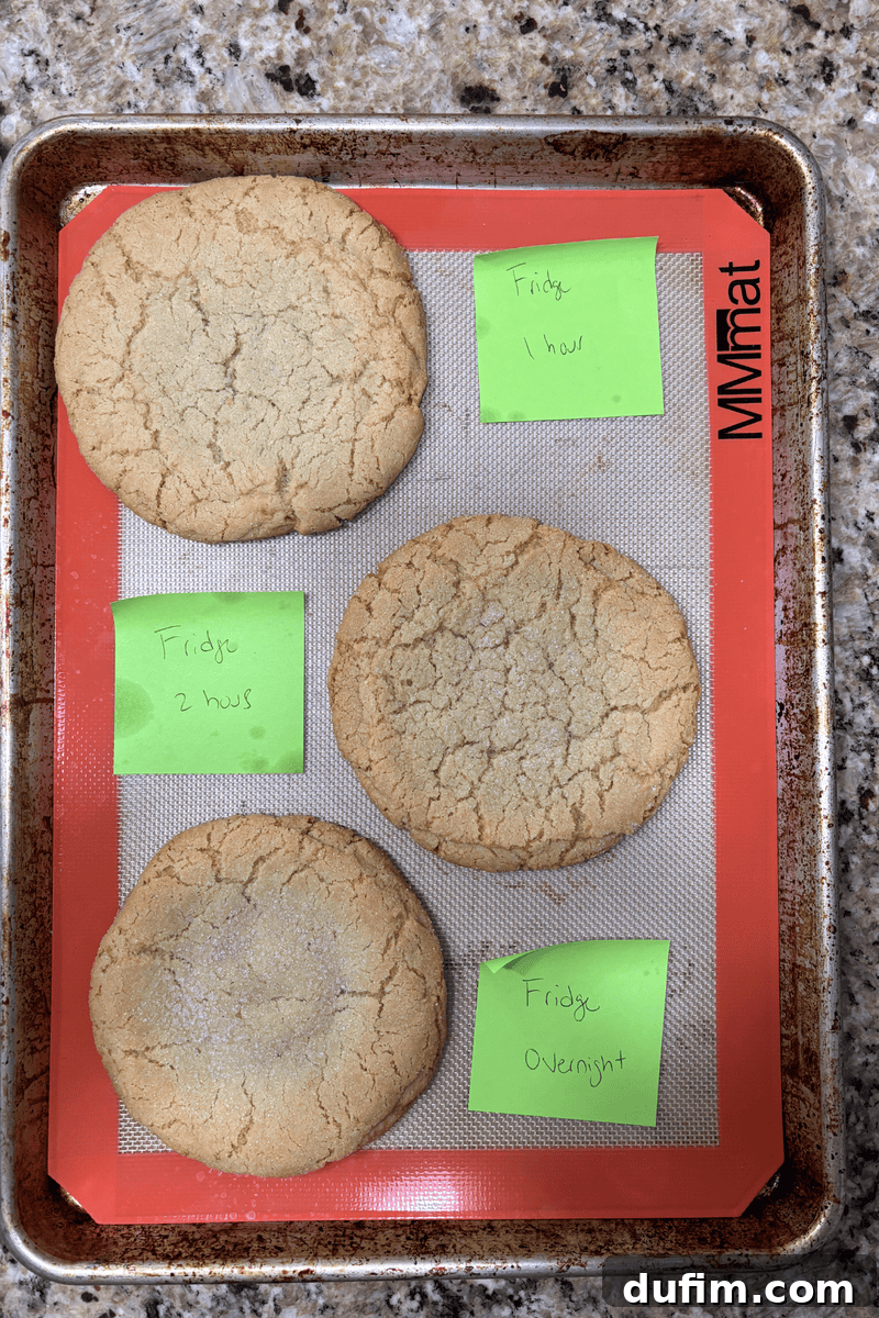 A baking tray with four large cookies on a silicone mat. Each cookie is labeled with a green sticky note.
