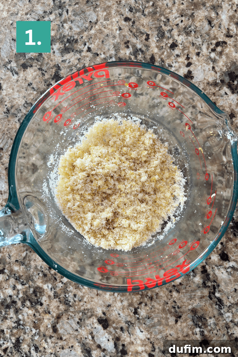 A glass measuring cup with a mixture of dry, crumbly ingredients sits on a speckled countertop.