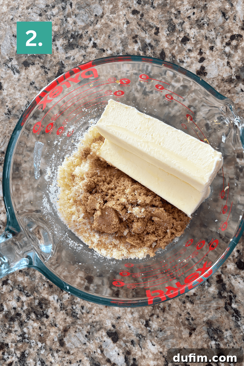 Two sticks of butter, brown sugar, and granulated sugar in a measuring cup on a counter.