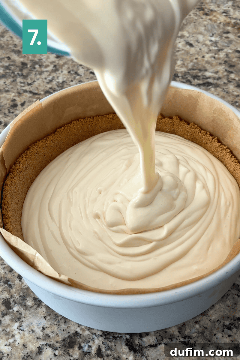 Strawberry Cheesecake Recipe with Fresh Strawberry Topping 10 A creamy cheesecake filling is being poured into a round pan lined with parchment paper and a graham cracker crust.