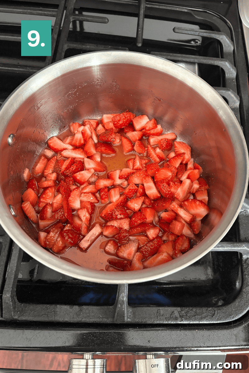 Strawberry Cheesecake Recipe with Fresh Strawberry Topping 12 A stainless steel pot with chopped strawberries and liquid simmering on a stovetop.