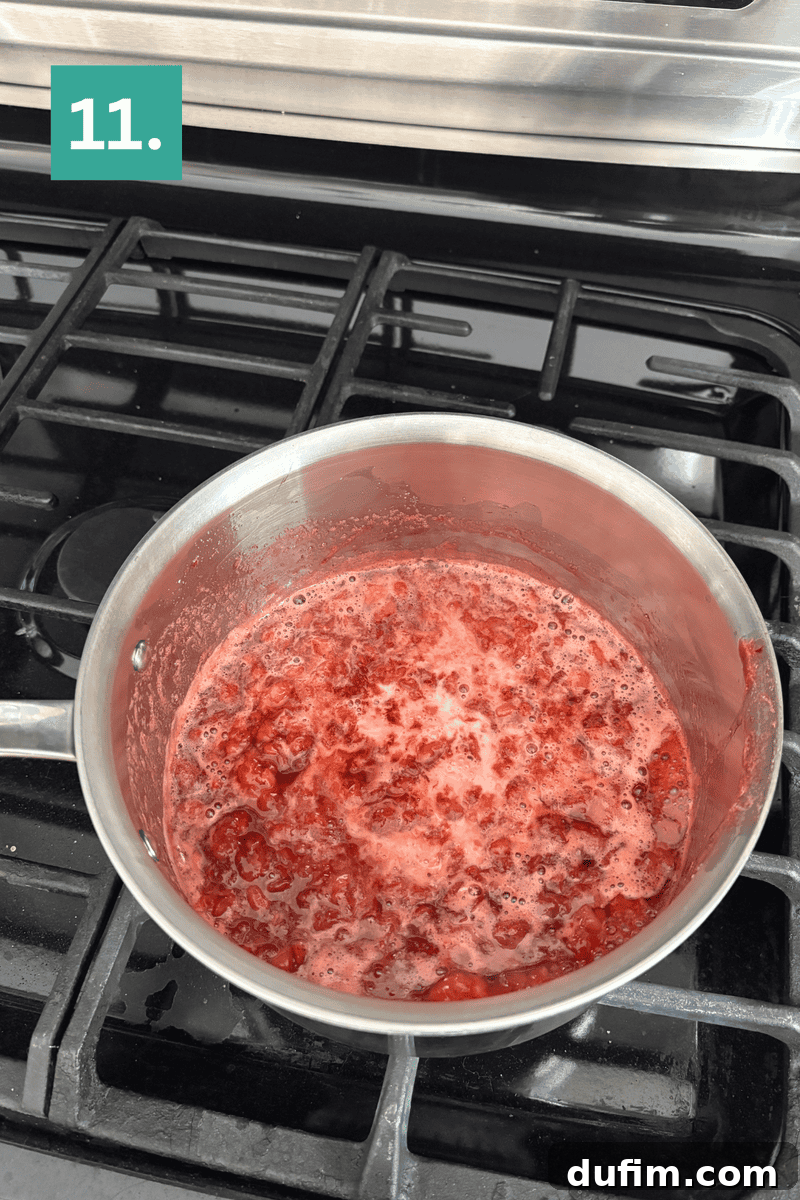 Strawberry Cheesecake Recipe with Fresh Strawberry Topping 14 A saucepan with bubbling, mashed red fruit mixture is on a stove.