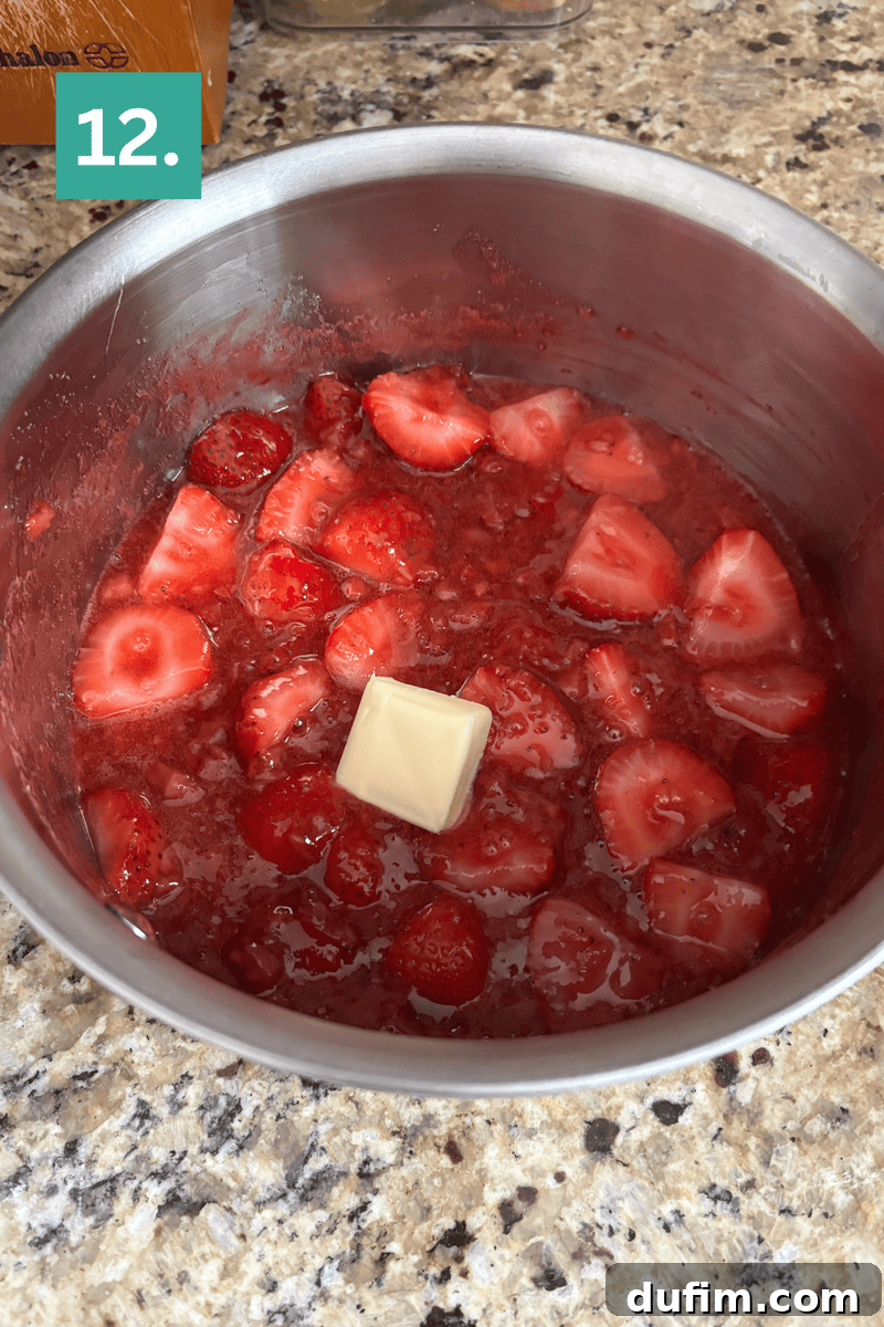 Strawberry Cheesecake Recipe with Fresh Strawberry Topping 15 A metal pot contains sliced strawberries in a red sauce with a pat of butter melting on top.