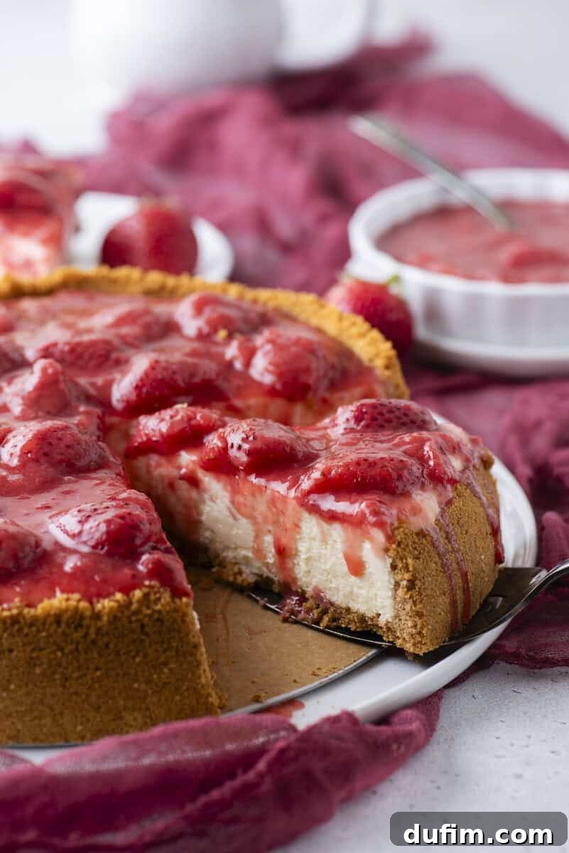 Strawberry Cheesecake Recipe with Fresh Strawberry Topping 17 A cheesecake with a golden crust topped with strawberries and strawberry sauce, with one slice removed.