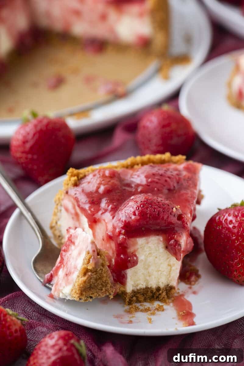 Strawberry Cheesecake Recipe with Fresh Strawberry Topping 18 A slice of cheesecake topped with strawberry sauce and fresh strawberries on a white plate with a fork.