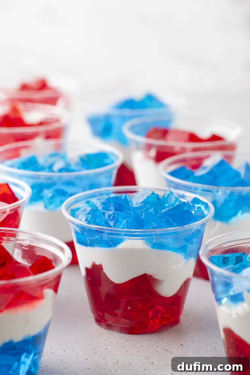 Clear plastic cups filled with layered red and blue gelatin and white creamy filling, arranged on a light surface for a festive, patriotic dessert display.
