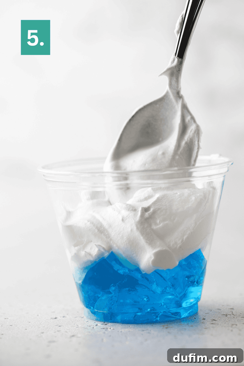 A plastic cup filled with blue gelatin and topped with a generous scoop of whipped cream. A spoon is inserted into the whipped cream.