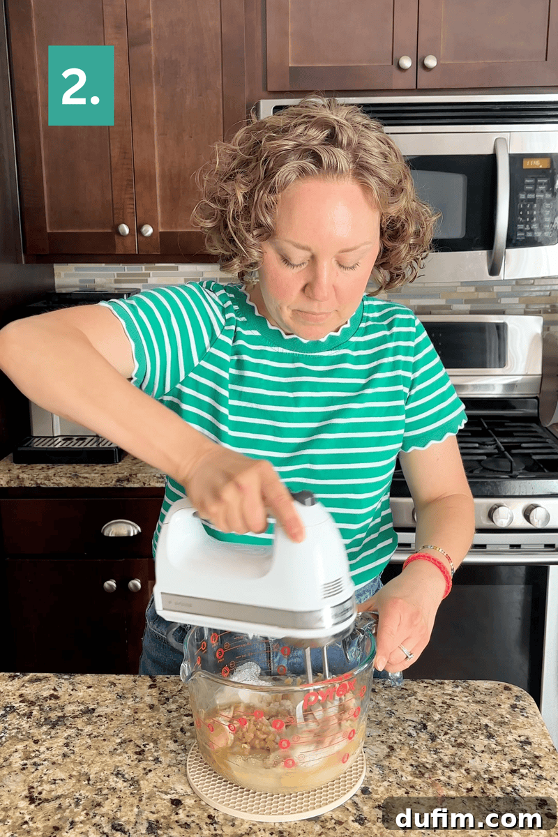 Peanut Butter Cake with Chocolate Frosting Recipe 8 A person in a green striped shirt uses a hand mixer in a glass bowl in a kitchen.
