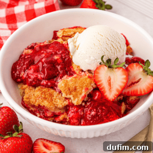 A white bowl filled with strawberry cobbler topped with a scoop of vanilla ice cream and fresh strawberry halves.