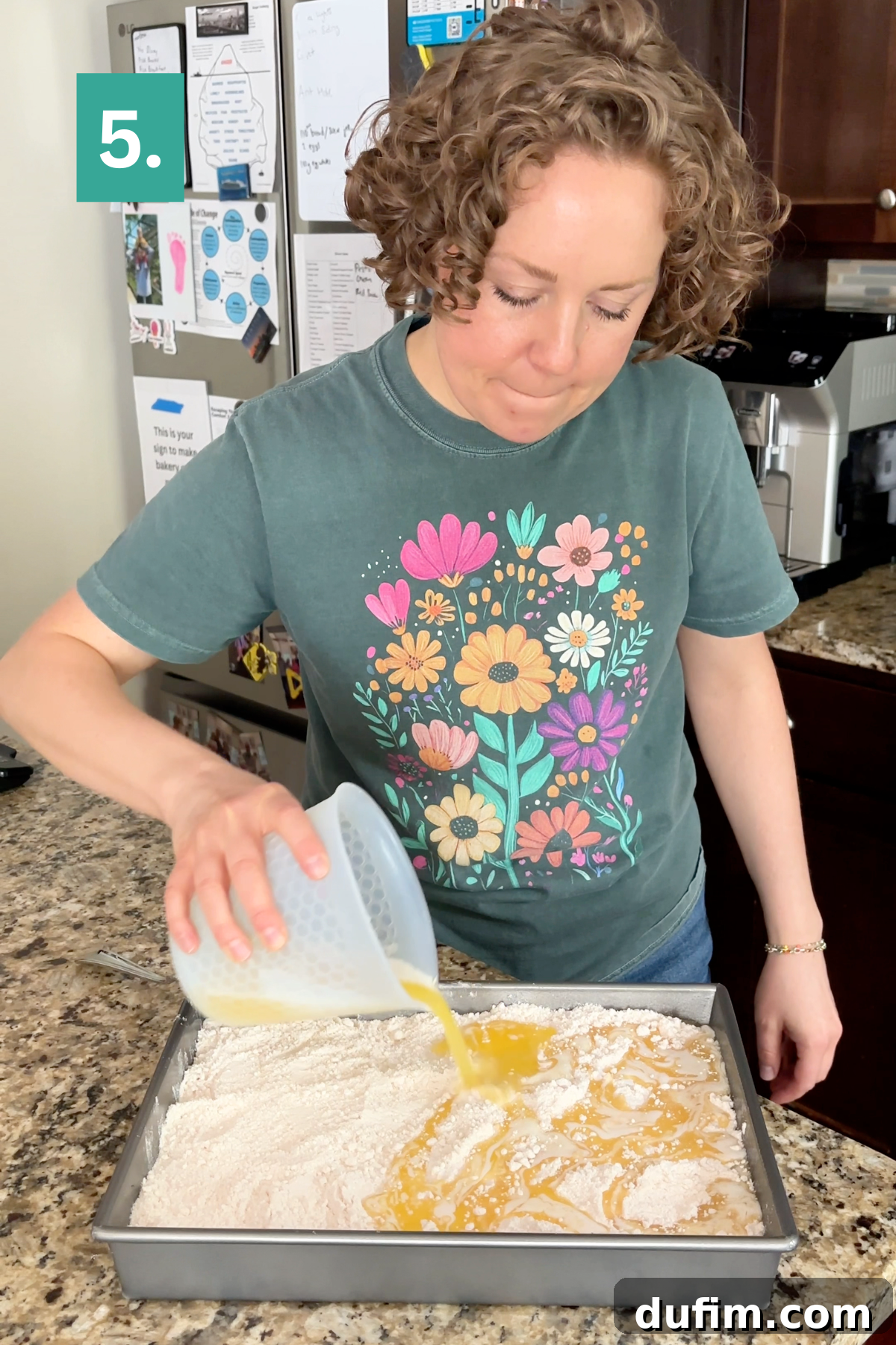 A person pours melted butter over the cake mix in a pan.