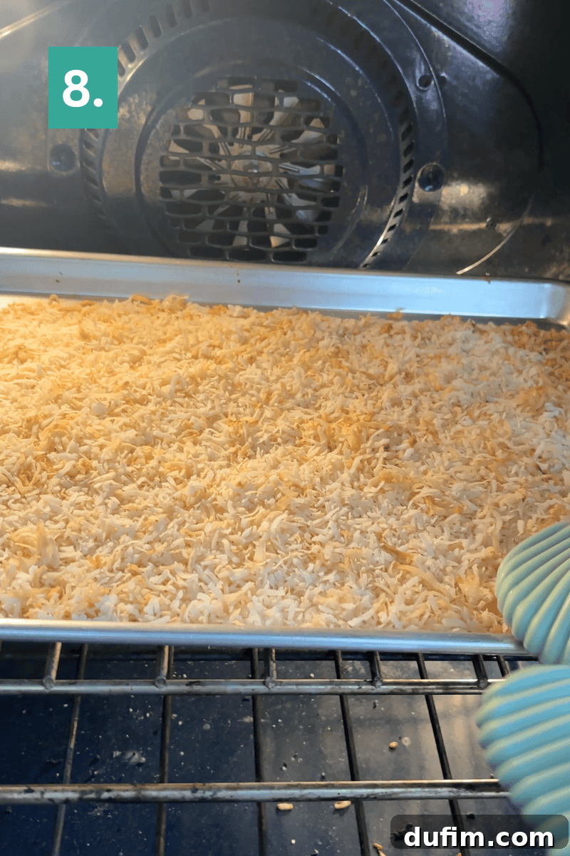 Homemade Coconut Cake That Tastes Like Real Coconut 9 A hand in an oven mitt pulls a baking sheet with toasted shredded coconut from an oven.