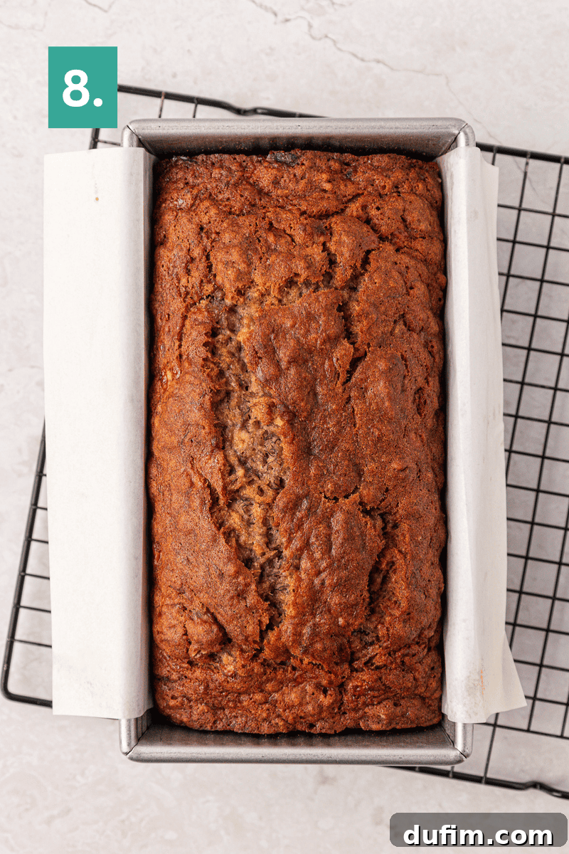Moist Gluten-Free Banana Bread Recipe 13 A loaf of banana bread in a parchment-lined metal pan sits on a cooling rack.