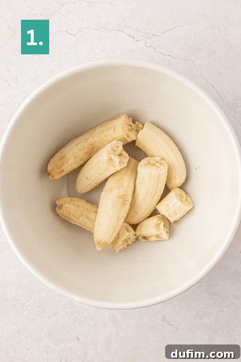 Moist Gluten-Free Banana Bread Recipe 6 A white bowl containing peeled and halved bananas sits on a light-colored surface.