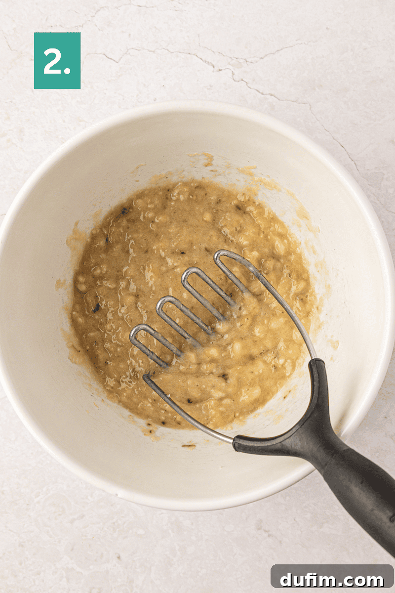 Moist Gluten-Free Banana Bread Recipe 7 A bowl of mashed bananas with a potato masher inside.