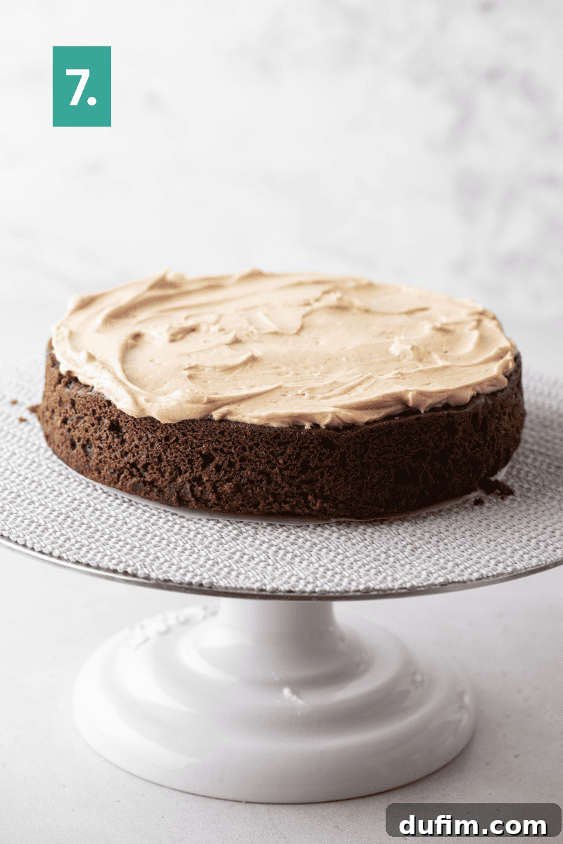 Decadent Mocha Cake Recipe for Coffee Lovers 13 A round chocolate cake with light brown frosting sits on a white cake stand. There is a green square with the number 7 in the upper left corner.