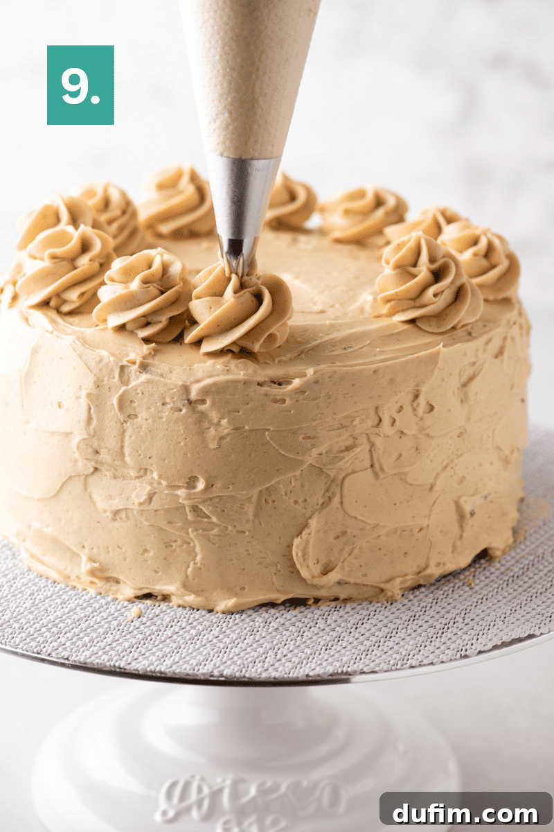 Decadent Mocha Cake Recipe for Coffee Lovers 15 A piping bag adds swirls of light brown frosting to the top of a round cake on a white stand, with a green box showing the number 9 in the corner.