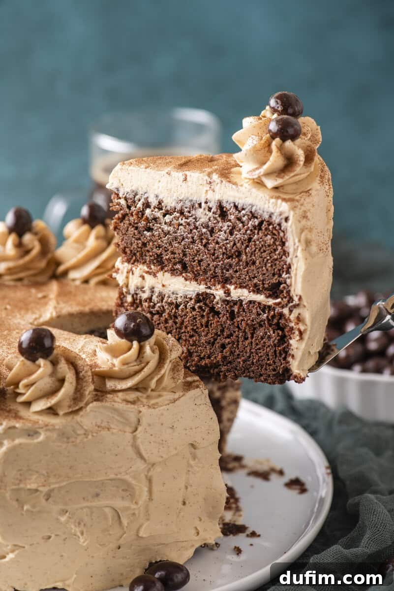 Decadent Mocha Cake Recipe for Coffee Lovers 17 A slice of two-layer chocolate cake with light brown frosting and chocolate decorations is being lifted from a frosted cake on a white plate.