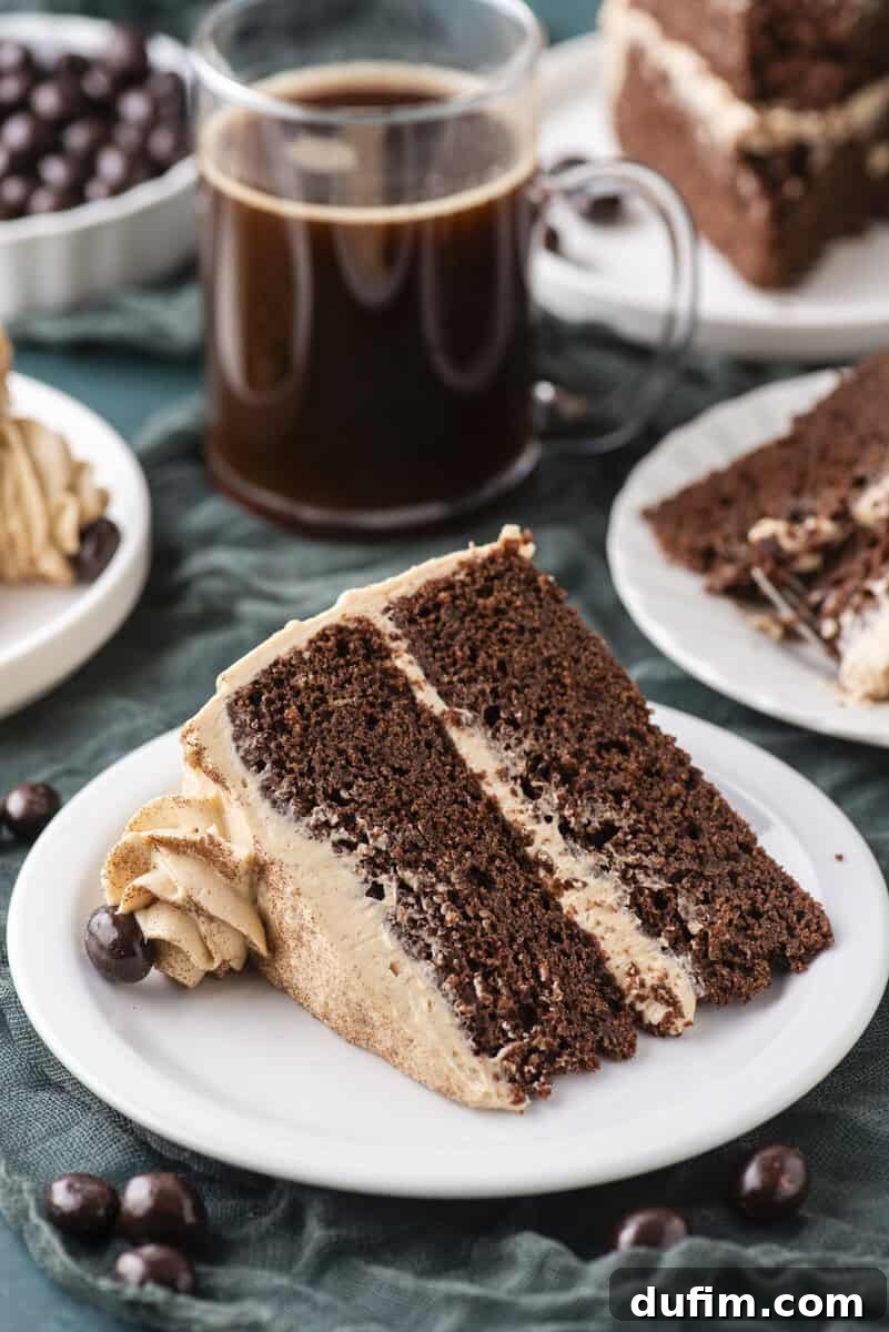 Decadent Mocha Cake Recipe for Coffee Lovers 18 A slice of chocolate layer cake with light brown frosting on a white plate, next to a glass mug of black coffee and chocolate-covered coffee beans. More cake slices are visible in the background.