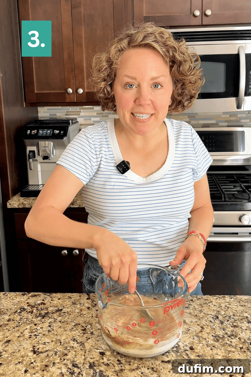Decadent Mocha Cake Recipe for Coffee Lovers 9 A woman wearing a striped shirt stirs ingredients in a glass measuring cup on a kitchen counter. A number 3. is shown in a green box in the corner.