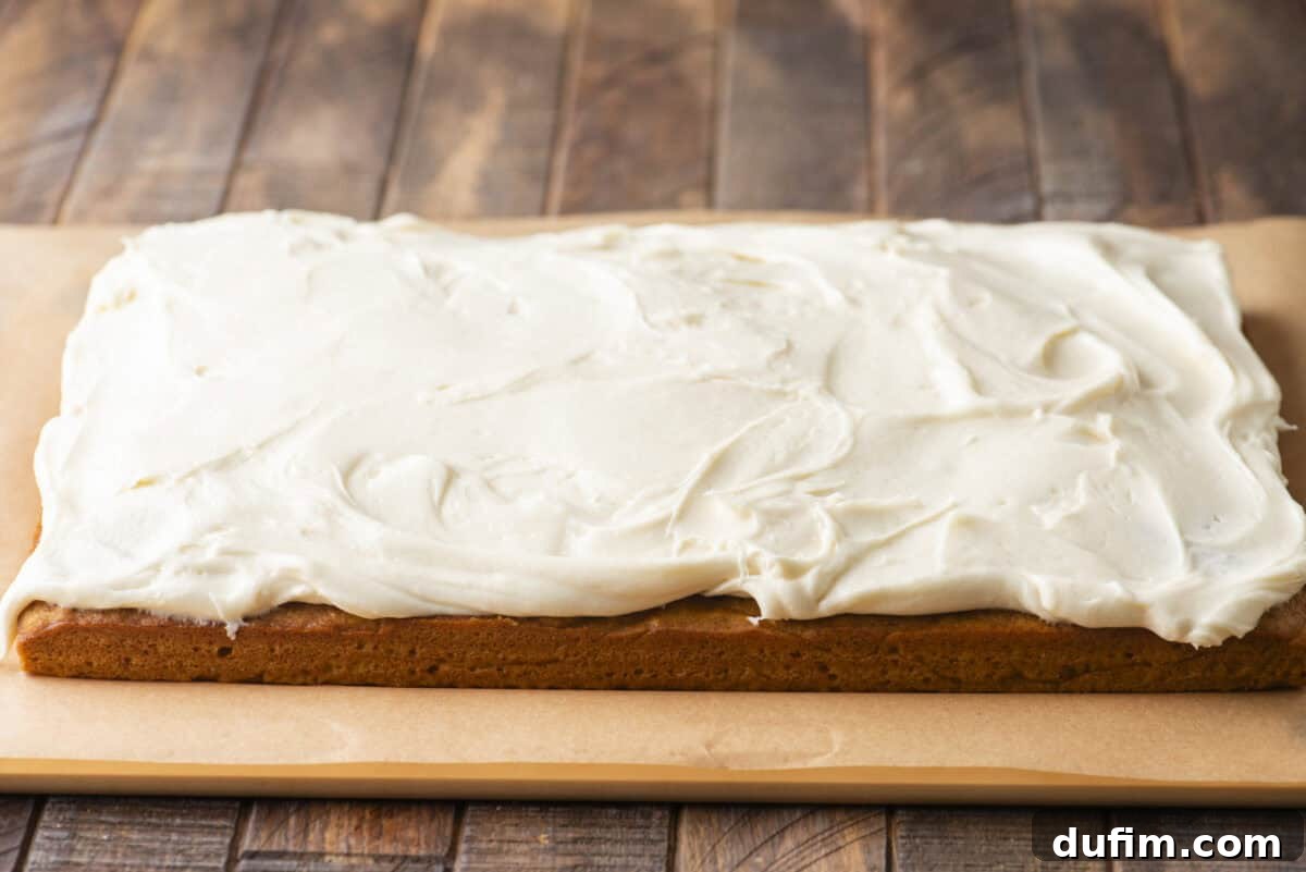 A rectangular sheet cake on parchment paper, topped with a thick, even layer of creamy white frosting, sits on a wooden surface.